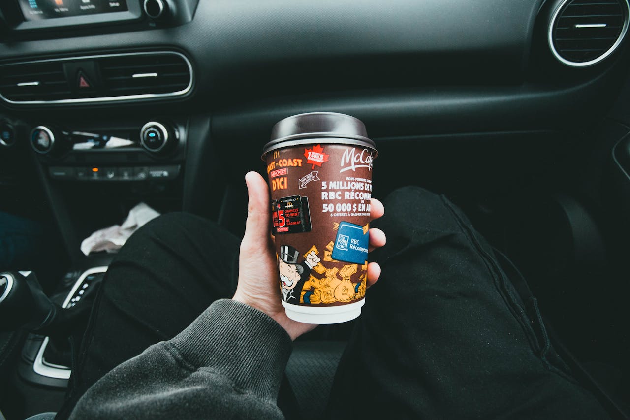 Close-up of a hand holding a McCafé coffee cup inside a car, capturing the cozy and casual travel vibe.