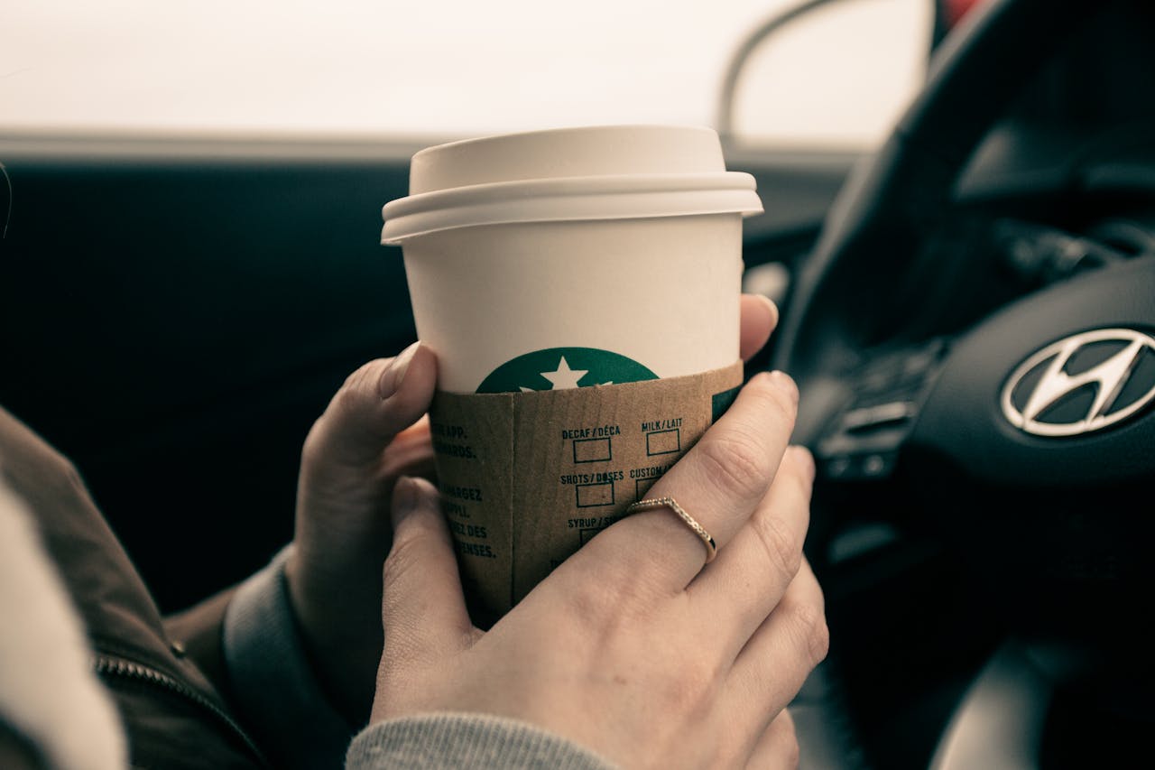 heros-img Close-up of hands holding a coffee cup inside a car, showcasing a modern lifestyle moment.